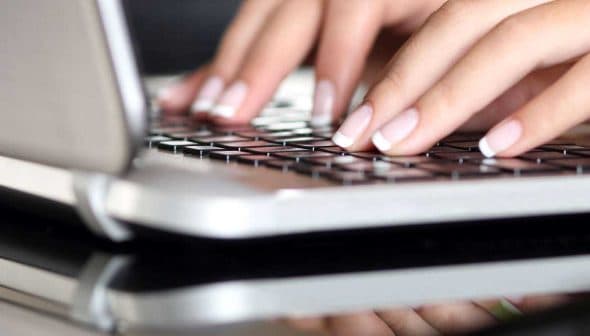 Close-up of hands typing on a laptop keyboard with a reflective surface. - Olive Oil Times