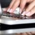 Close-up of hands typing on a laptop keyboard with a reflective surface. - Olive Oil Times