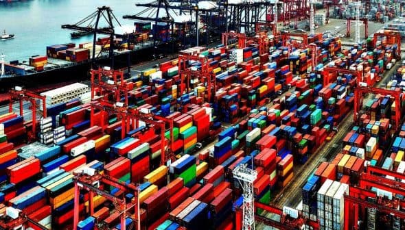 Aerial view of a container ship docked at a port surrounded by colorful shipping containers. - Olive Oil Times
