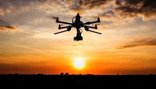 Silhouette of a drone flying against a sunset with clouds in the sky. - Olive Oil Times