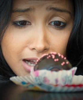A woman with dark hair gazing intently at a chocolate dessert on a plate. - Olive Oil Times