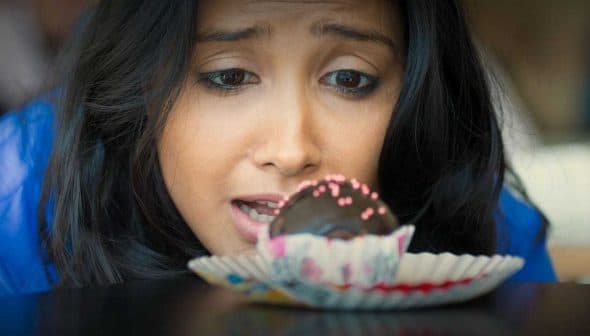 A woman with dark hair gazing intently at a chocolate dessert on a plate. - Olive Oil Times