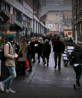People walking through a narrow urban passageway with shops on either side. - Olive Oil Times