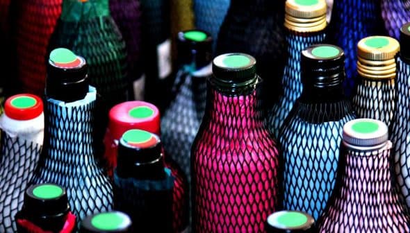 Various bottles with colorful netting and caps in a close-up view. - Olive Oil Times