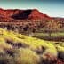 A red rock formation surrounded by grassland and sparse trees under a clear sky. - Olive Oil Times
