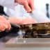 Chef in a white shirt using a frying pan on a gas stove in a kitchen setting. - Olive Oil Times