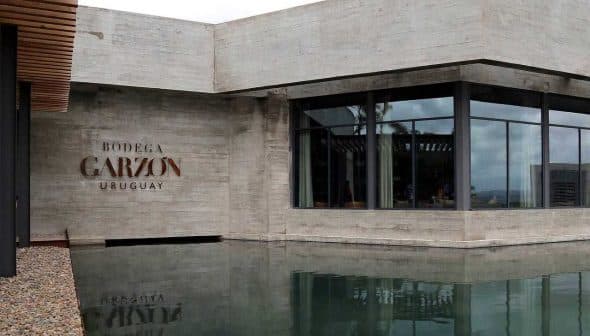 Modern architectural structure of Bodega Garzon with water reflection in front. - Olive Oil Times