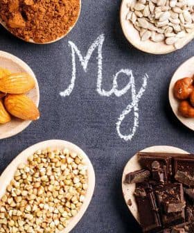 Wooden spoons containing almonds, hazelnuts, sunflower seeds, and cocoa powder arranged around the letter 'Mg' written in chalk. - Olive Oil Times