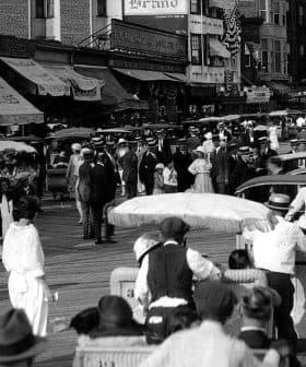 Black and white photograph of a busy boardwalk filled with pedestrians and horse-drawn carriages. - Olive Oil Times