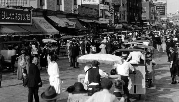 Black and white photograph of a busy boardwalk filled with pedestrians and horse-drawn carriages. - Olive Oil Times