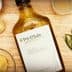 Bottle of olive oil labeled 'Pot d'Huile' with garlic, mustard, and herbs on a wooden surface. - Olive Oil Times