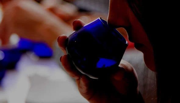 Individual holding a blue glass container while smelling olive oil during a tasting session. - Olive Oil Times