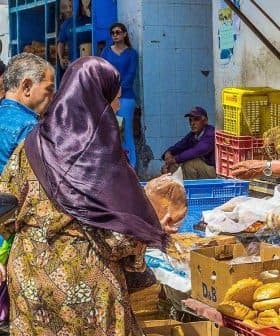 A busy market scene featuring vendors selling baked goods and shoppers browsing at stalls. - Olive Oil Times