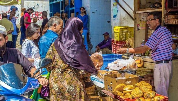 A busy market scene featuring vendors selling baked goods and shoppers browsing at stalls. - Olive Oil Times