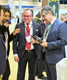 Four individuals engaged in conversation while examining olive oil products at an event. - Olive Oil Times