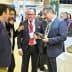 Four individuals engaged in conversation while examining olive oil products at an event. - Olive Oil Times