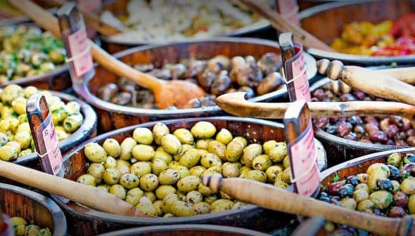 Multiple wooden bowls filled with different types of olives, each with a wooden spoon for serving. - Olive Oil Times