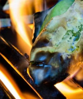 Green peppers being grilled on a barbecue grill with flames visible. - Olive Oil Times