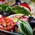 A bowl of mixed salad featuring cherry tomatoes, black olives, and fresh basil leaves. - Olive Oil Times
