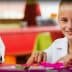 Two children smiling while eating lunch at a colorful table in a dining area. - Olive Oil Times