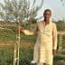 Man in traditional attire standing beside a young olive tree in a field. - Olive Oil Times