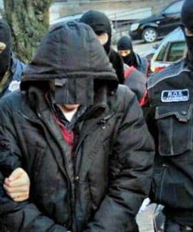 Police officers in tactical gear escorting an individual wearing a hooded jacket. - Olive Oil Times