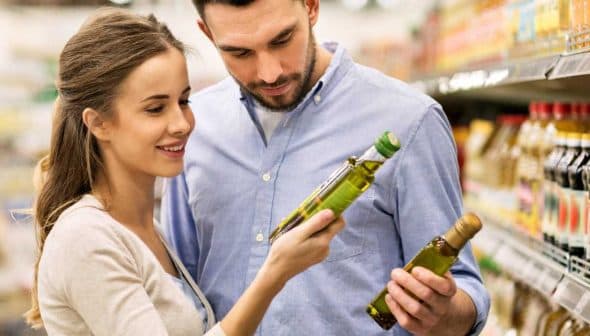 A couple inspecting olive oil bottles while shopping in a supermarket aisle. - Olive Oil Times