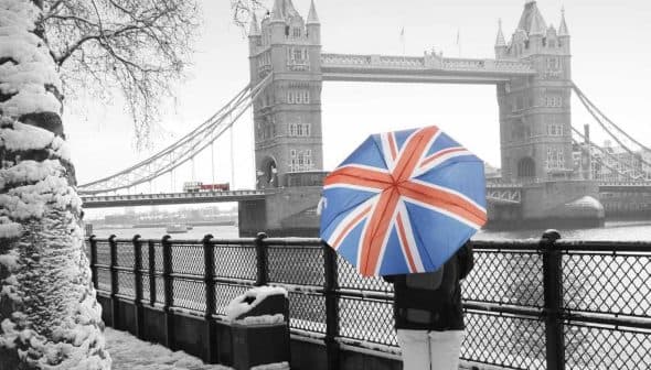 Individual holding a Union Jack umbrella while standing near Tower Bridge in winter. - Olive Oil Times