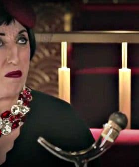 Woman seated at a restaurant wearing a black dress and a large statement necklace with red and silver accents. - Olive Oil Times