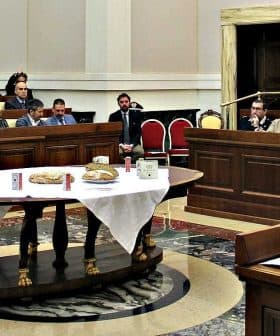 A legislative assembly room with attendees seated at tables during a meeting. - Olive Oil Times