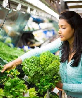 Woman with long black hair selecting fresh greens from a grocery store display. - Olive Oil Times