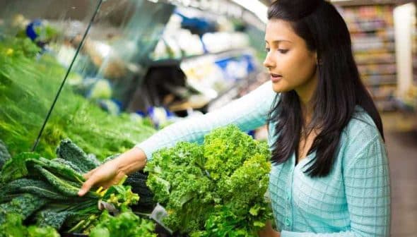 Woman with long black hair selecting fresh greens from a grocery store display. - Olive Oil Times
