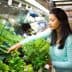 Woman with long black hair selecting fresh greens from a grocery store display. - Olive Oil Times