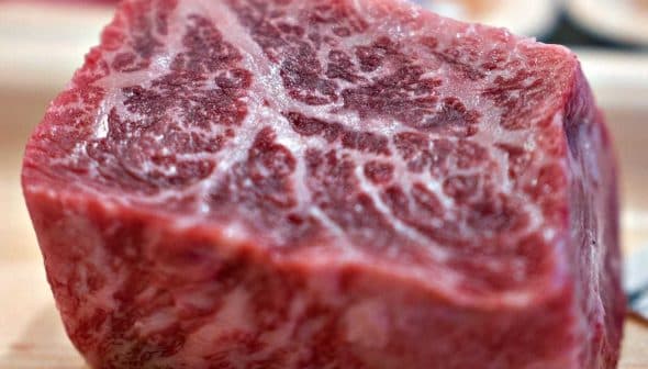 A close-up view of a raw beef cut showcasing marbling in the meat. - Olive Oil Times