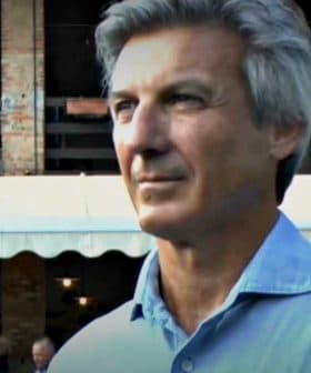 A man with gray hair wearing a light blue shirt, standing outdoors in a casual setting. - Olive Oil Times