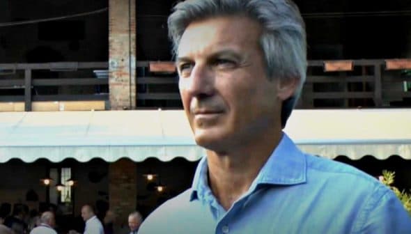 A man with gray hair wearing a light blue shirt, standing outdoors in a casual setting. - Olive Oil Times