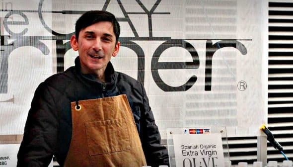 Man wearing an apron standing behind a table at an olive oil tasting event. - Olive Oil Times