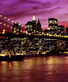 Brooklyn Bridge illuminated at night with the New York City skyline in the background under a purple sky. - Olive Oil Times