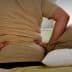 Individual sitting on a bed with hands on lower back, indicating discomfort or pain. - Olive Oil Times