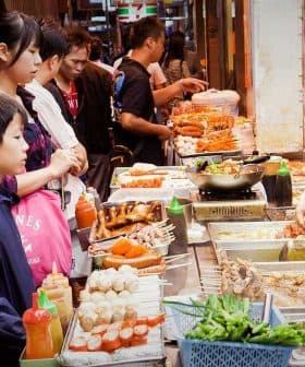 A street food vendor serving various dishes to a group of customers in a market setting. - Olive Oil Times