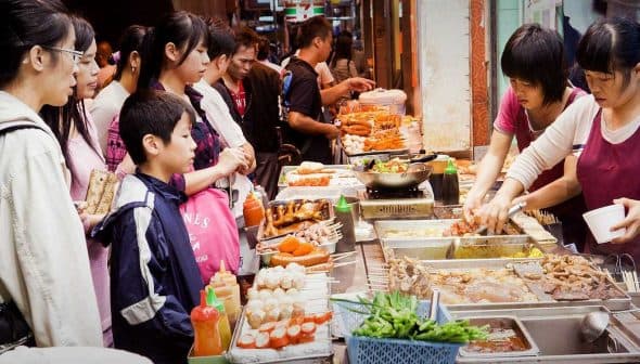 A street food vendor serving various dishes to a group of customers in a market setting. - Olive Oil Times