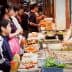 A street food vendor serving various dishes to a group of customers in a market setting. - Olive Oil Times