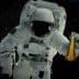 An astronaut in a space suit holding a flask filled with a yellow liquid while floating in space. - Olive Oil Times