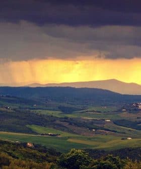 Panoramic view of rolling hills with dark clouds and sunlight breaking through in the distance. - Olive Oil Times