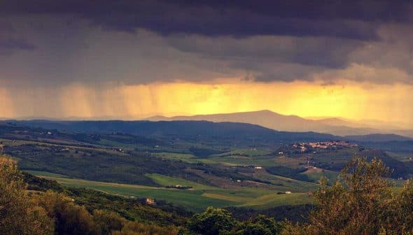 Panoramic view of rolling hills with dark clouds and sunlight breaking through in the distance. - Olive Oil Times
