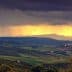 Panoramic view of rolling hills with dark clouds and sunlight breaking through in the distance. - Olive Oil Times