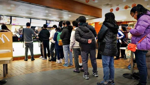 A group of people standing in line at a McDonald's restaurant waiting to order. - Olive Oil Times