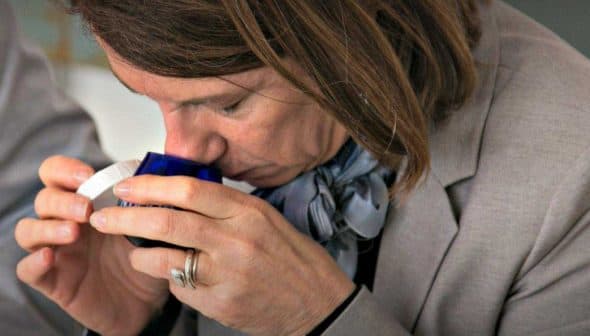 Individual smelling a small blue container during an olive oil tasting session. - Olive Oil Times