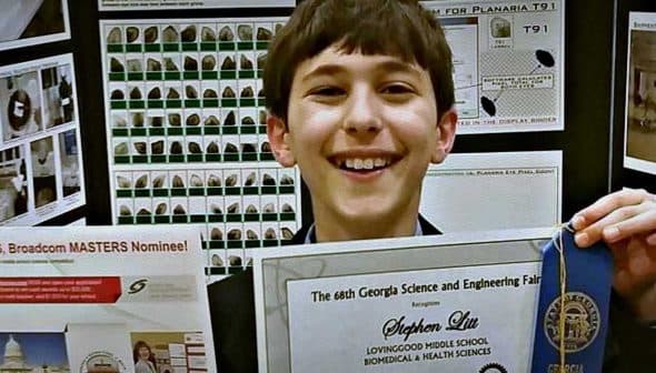 Young student holding a certificate and ribbon at a science and engineering fair. - Olive Oil Times