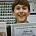 Young student holding a certificate and ribbon at a science and engineering fair. - Olive Oil Times